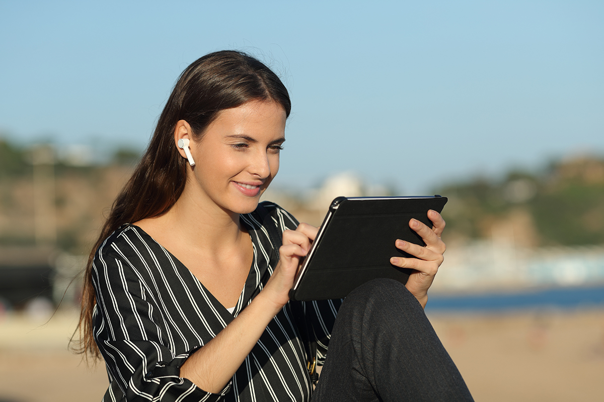 Casual donna felice e-learning con tablet e auricolari wireless seduti sulla spiaggia